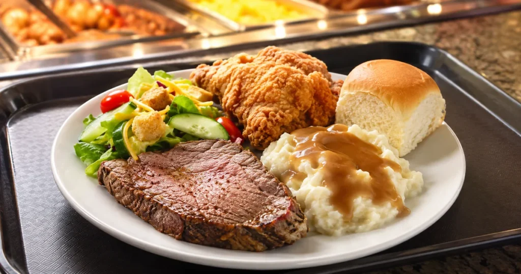 Is Golden Corral Worth It in 2026? An Honest Cost vs Value Verdict 1 Close-up of a loaded buffet plate with sirloin steak, fried chicken, mashed potatoes with gravy, fresh salad, and a soft dinner roll on a restaurant tray under warm lighting.